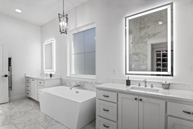 full bath with a soaking tub, marble finish floor, two vanities, and a sink