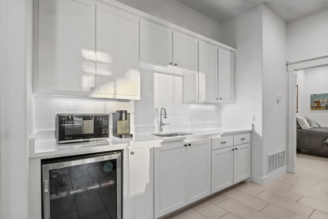 kitchen featuring wine cooler, a sink, light countertops, white cabinetry, and backsplash