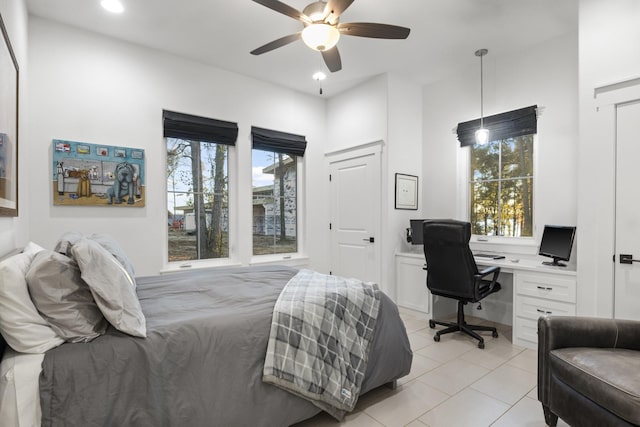 bedroom with light tile patterned floors, ceiling fan, built in desk, and multiple windows