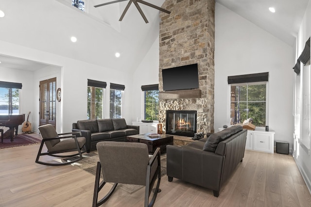 living room with light wood-style floors, recessed lighting, high vaulted ceiling, and a stone fireplace