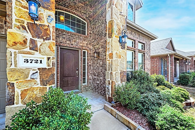 doorway to property with a garage, stone siding, and brick siding