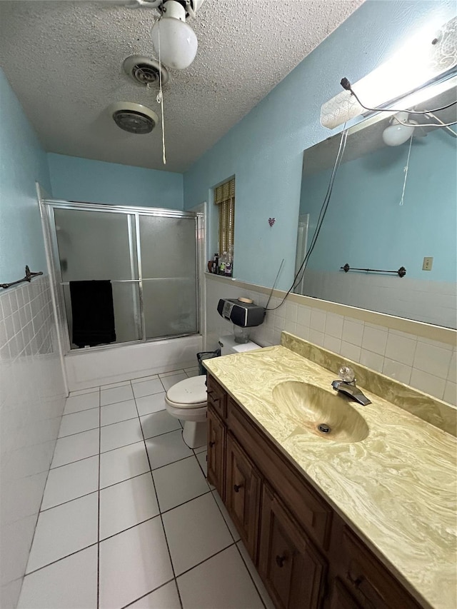 bathroom featuring bath / shower combo with glass door, tile patterned flooring, a textured ceiling, vanity, and tile walls