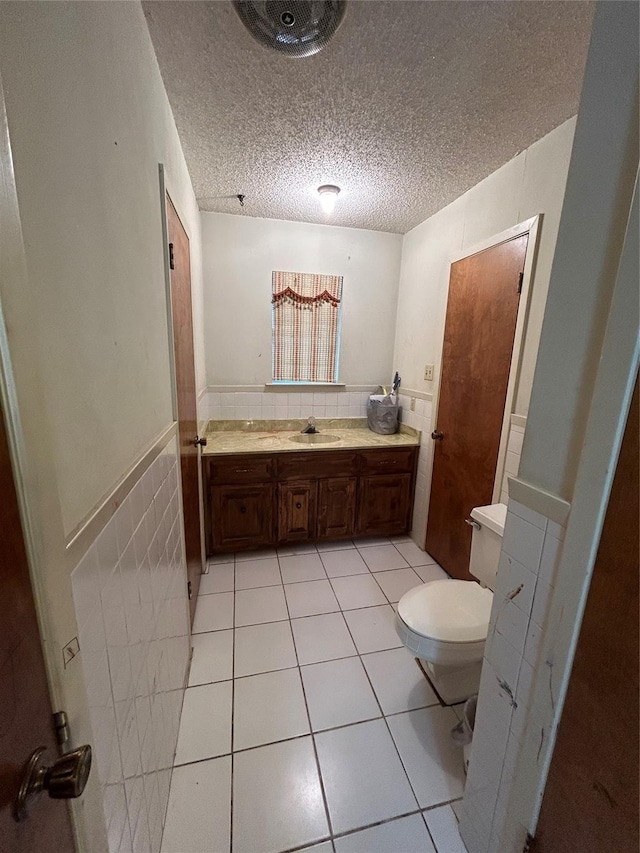 bathroom with tile patterned flooring, wainscoting, tile walls, and a textured ceiling