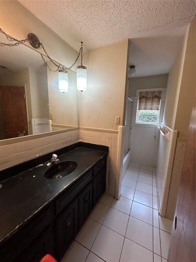 full bath with a textured ceiling, tile patterned flooring, vanity, tile walls, and wainscoting