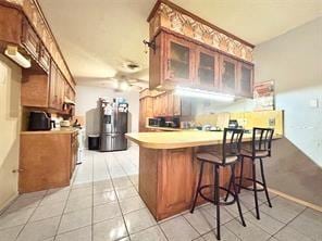 kitchen featuring a peninsula, glass insert cabinets, brown cabinetry, and light tile patterned flooring