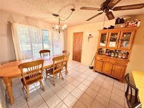 dining space with a textured ceiling, light tile patterned floors, and ceiling fan with notable chandelier