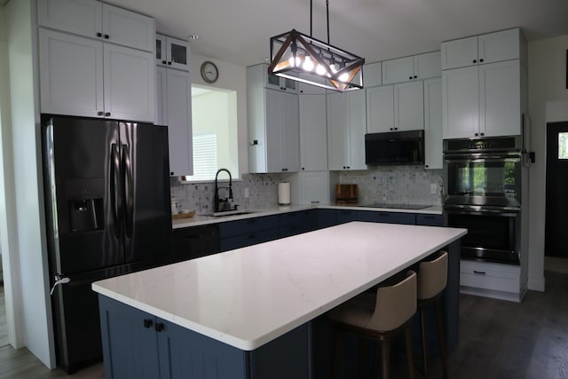 kitchen featuring black appliances, decorative backsplash, a sink, and a center island