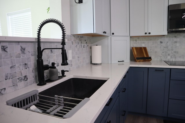 kitchen featuring light stone counters, tasteful backsplash, white cabinets, a sink, and black electric cooktop