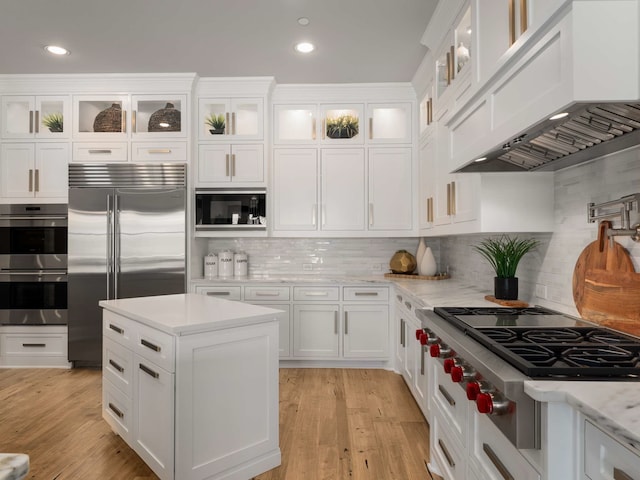 kitchen featuring light wood finished floors, built in appliances, custom exhaust hood, and white cabinetry