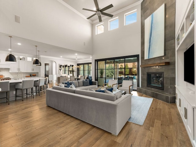 living room featuring ceiling fan, ornamental molding, a fireplace, light wood-style floors, and arched walkways