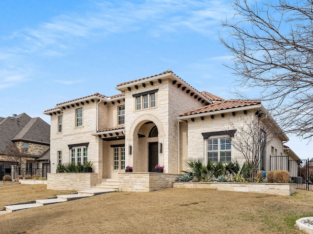 mediterranean / spanish home with a front yard, a tiled roof, fence, and stone siding