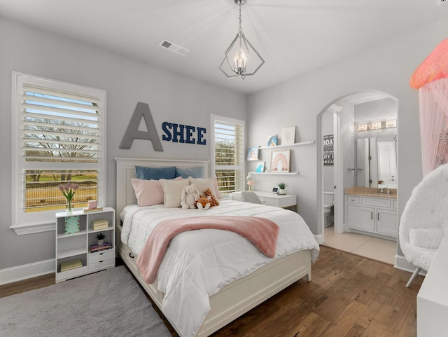 bedroom with visible vents, ensuite bathroom, wood finished floors, arched walkways, and baseboards