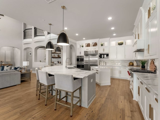 kitchen featuring a large island, a sink, backsplash, arched walkways, and built in appliances