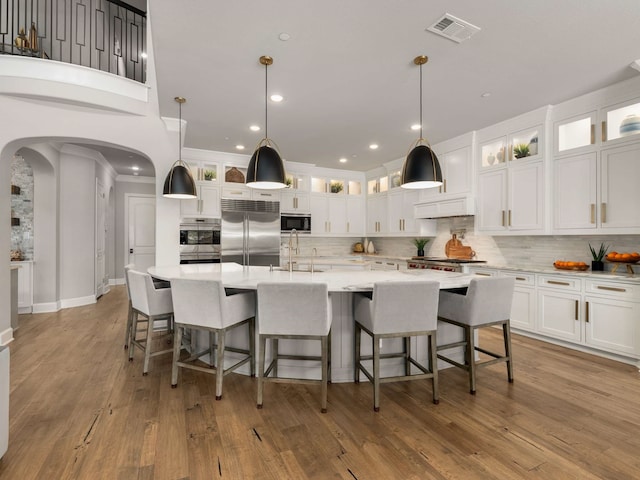 kitchen with visible vents, arched walkways, a sink, light countertops, and built in appliances