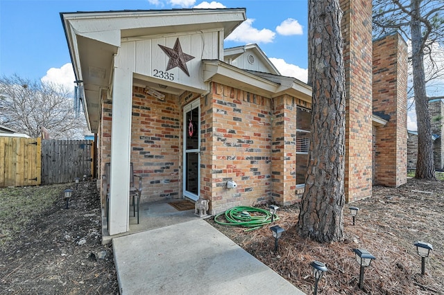 doorway to property with board and batten siding, brick siding, and fence