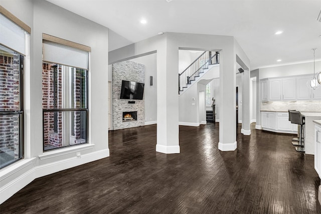 living room featuring dark wood-style floors, a glass covered fireplace, stairway, and baseboards