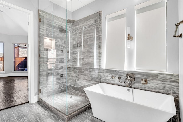 full bath featuring a stall shower, a freestanding tub, tile walls, and wood finished floors