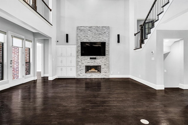 unfurnished living room with a stone fireplace, wood finished floors, and baseboards