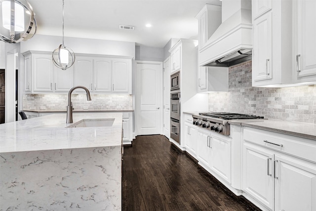 kitchen featuring light stone counters, custom exhaust hood, stainless steel appliances, visible vents, and a sink