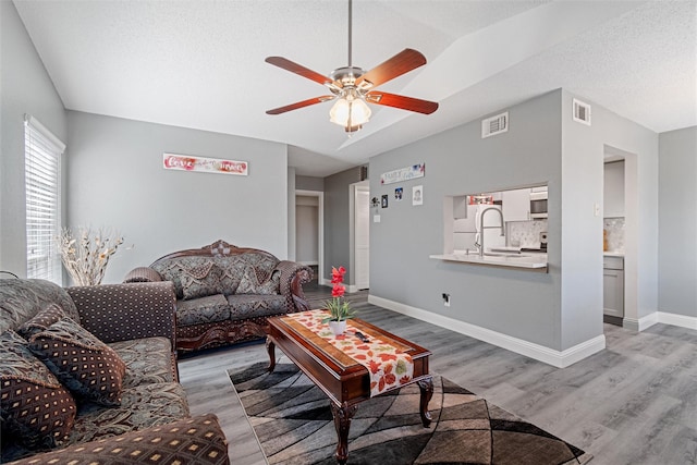 living area with a ceiling fan, baseboards, visible vents, and light wood finished floors