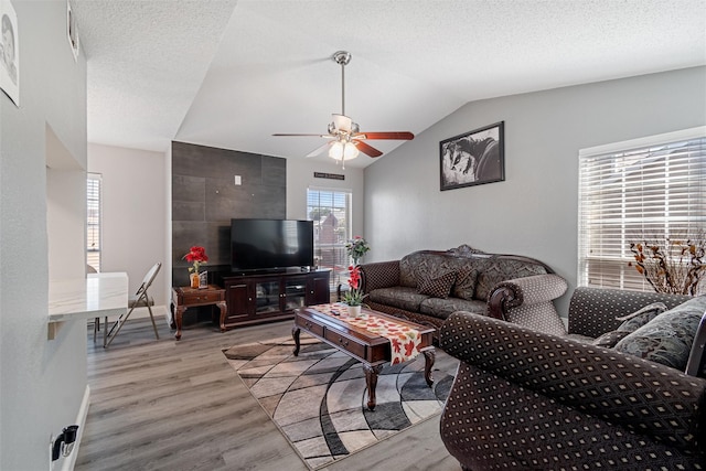 living room with vaulted ceiling, a textured ceiling, light wood finished floors, and ceiling fan