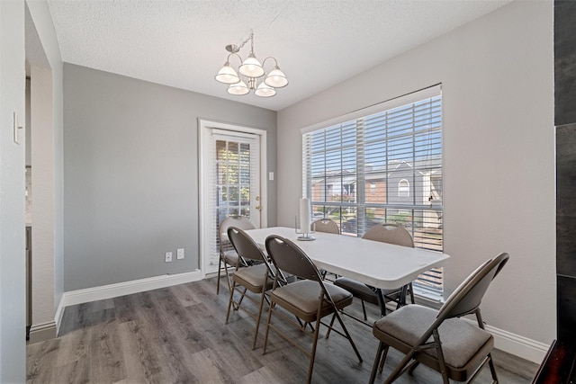 dining space with a chandelier, a textured ceiling, baseboards, and wood finished floors