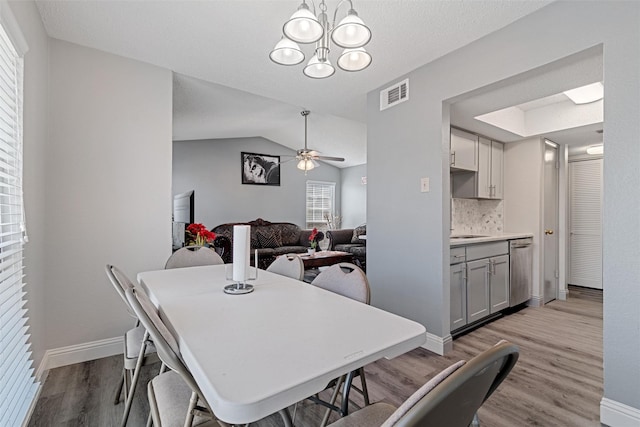 dining area with visible vents, vaulted ceiling, wood finished floors, baseboards, and ceiling fan with notable chandelier