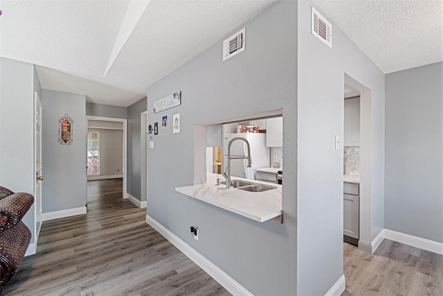 corridor with light wood finished floors, baseboards, visible vents, and a sink