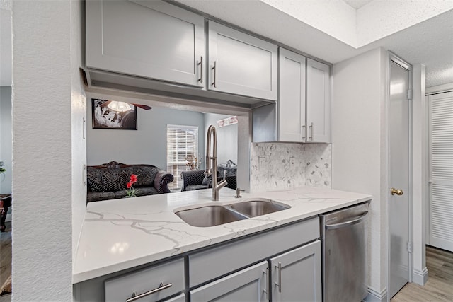 kitchen with gray cabinetry, a sink, light wood-type flooring, light stone countertops, and dishwasher