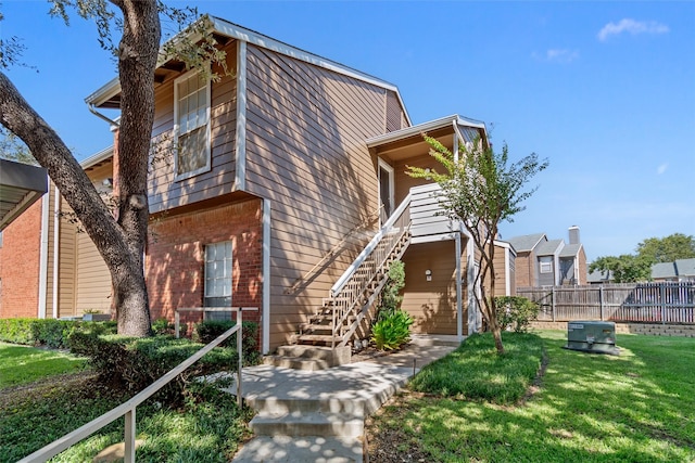 view of front of property featuring stairway, fence, a front lawn, and brick siding