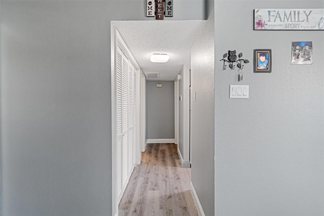 hallway with a textured ceiling, light wood finished floors, and baseboards