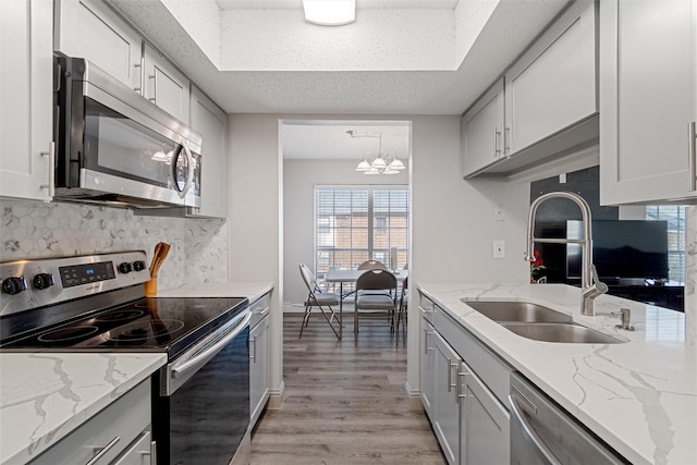 kitchen featuring decorative backsplash, light stone counters, stainless steel appliances, light wood-style floors, and a sink