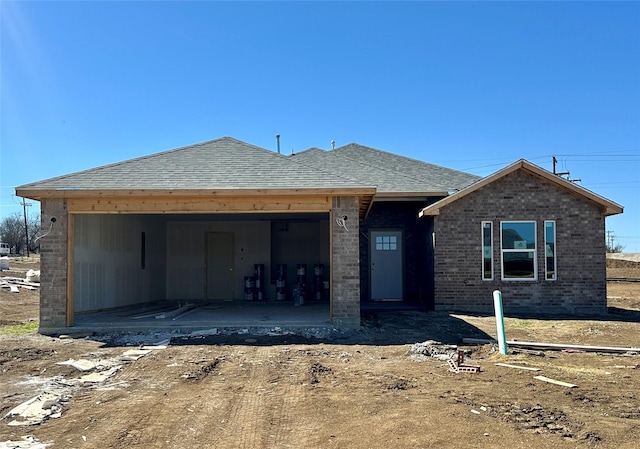 unfinished property with an attached garage, a patio area, a shingled roof, and brick siding