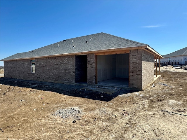 rear view of house featuring roof with shingles and brick siding