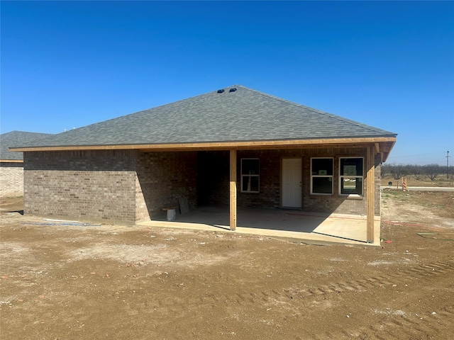 rear view of house featuring a shingled roof and brick siding