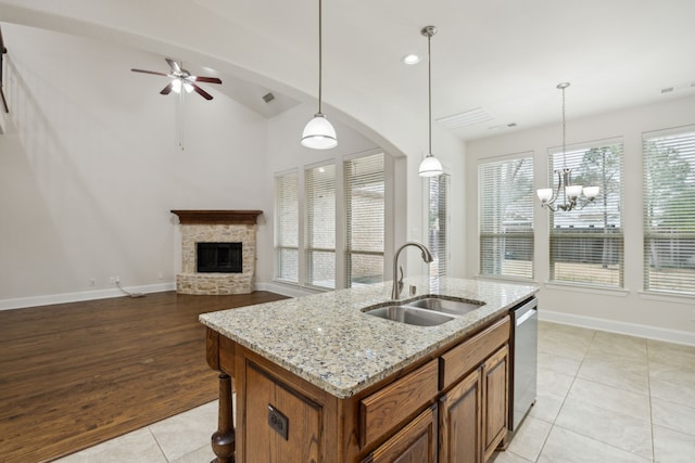 kitchen with stainless steel dishwasher, brown cabinetry, open floor plan, a sink, and a stone fireplace