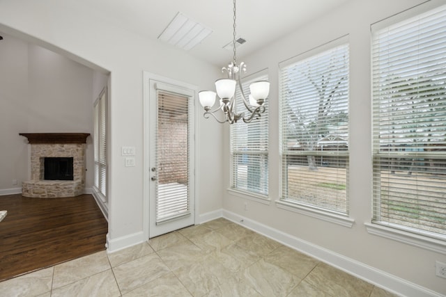 unfurnished dining area featuring light tile patterned flooring, baseboards, a notable chandelier, and a stone fireplace