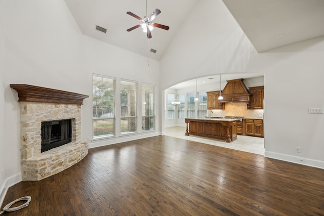 unfurnished living room with light wood-type flooring, a fireplace, visible vents, and a ceiling fan