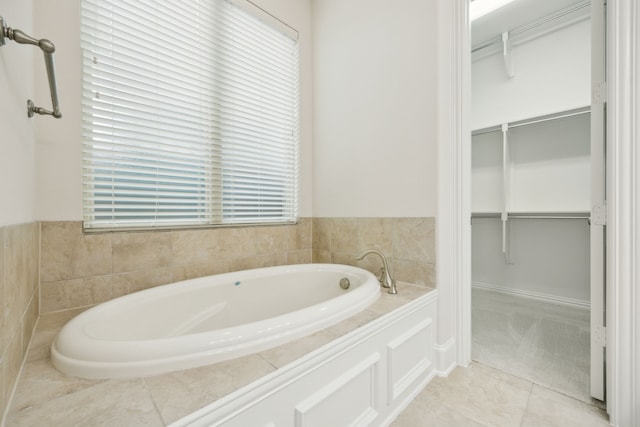 bathroom with a spacious closet, a garden tub, and tile patterned floors