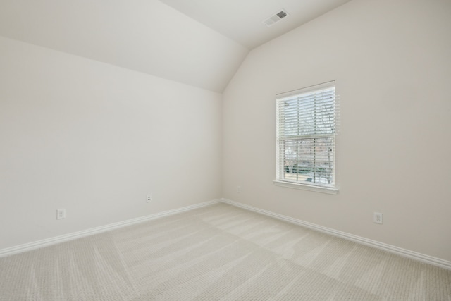 empty room featuring light carpet, baseboards, visible vents, and vaulted ceiling