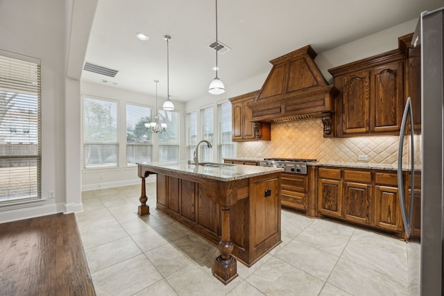 kitchen with light stone counters, tasteful backsplash, custom range hood, appliances with stainless steel finishes, and a sink