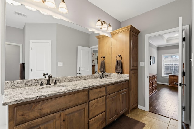 bathroom with a raised ceiling, double vanity, a sink, and visible vents