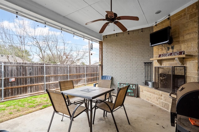 view of patio / terrace with area for grilling, ceiling fan, fence, an outdoor stone fireplace, and outdoor dining space