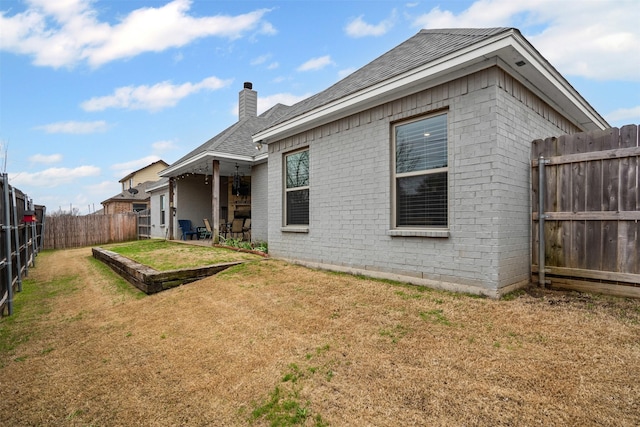 rear view of house featuring a fenced backyard, brick siding, a yard, a chimney, and a patio area