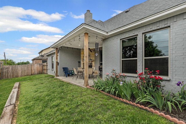 back of property with fence, a chimney, brick siding, a patio area, and a lawn