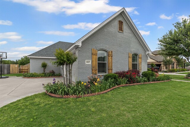 view of side of property with fence, roof with shingles, brick siding, a lawn, and driveway