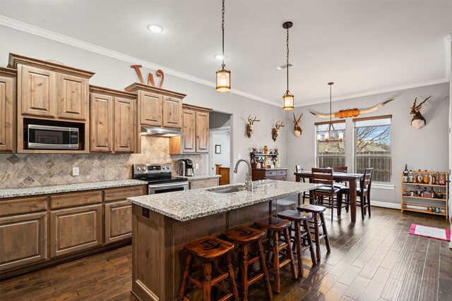 kitchen with crown molding, a sink, light stone counters, under cabinet range hood, and stainless steel appliances