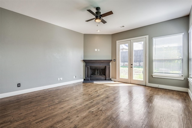 unfurnished living room featuring french doors, a fireplace with raised hearth, baseboards, and wood finished floors