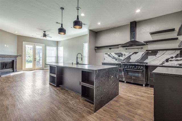 kitchen featuring range with two ovens, wall chimney exhaust hood, wood finished floors, open shelves, and a sink