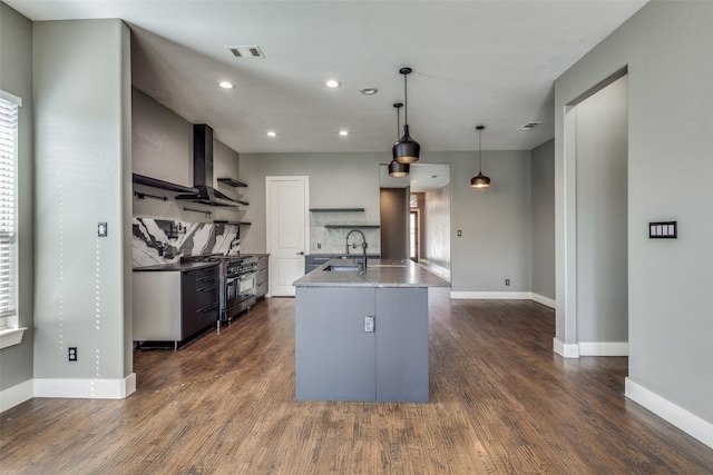 kitchen with decorative backsplash, dark wood-style floors, wall chimney exhaust hood, stainless steel range with gas cooktop, and a sink